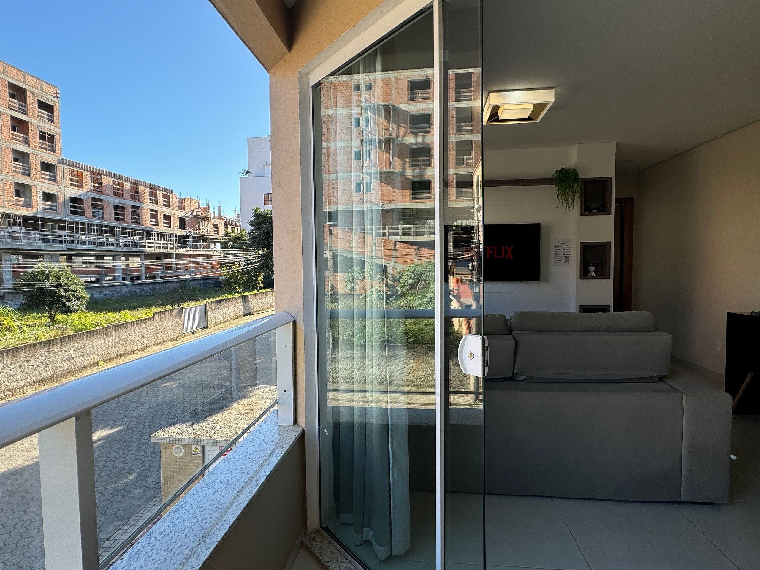 A modern apartment with a balcony, a sofa, and a glass door leading to a city view.