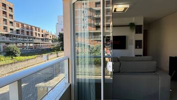 A modern apartment with a balcony, a sofa, and a glass door leading to a city view.