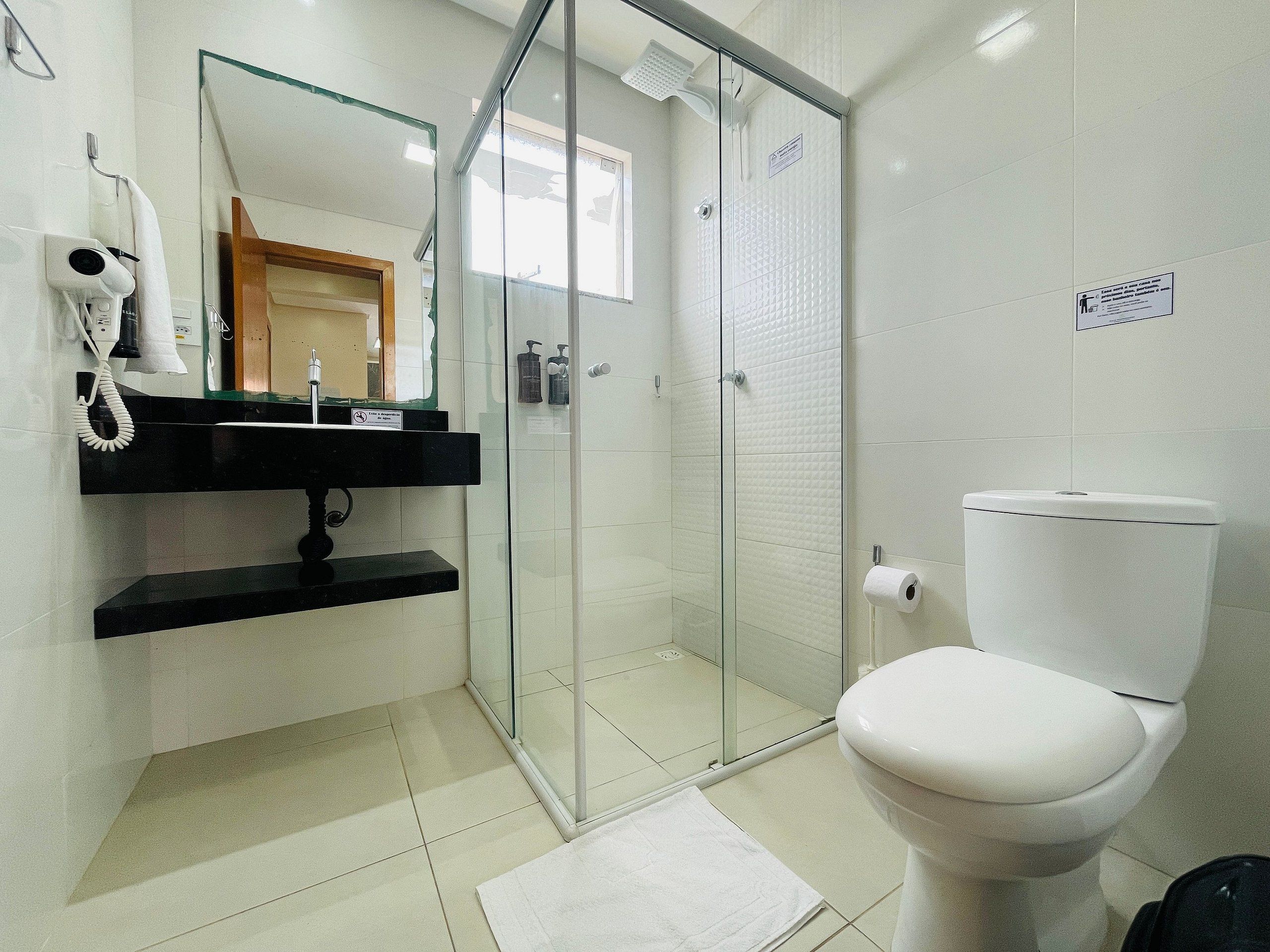 A modern bathroom with a glass-enclosed shower, a white toilet, and a black sink with a towel hanging on the wall.