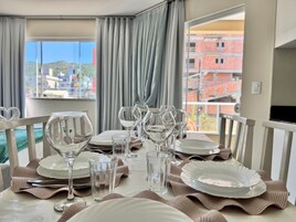 Mesa posta com pratos, copos e talheres, com vista para edifícios pela janela.