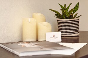 Trois bougies blanches, une plante en pot à rayures et une carte de visite sur une table.