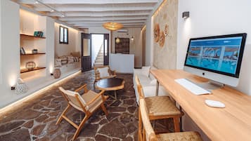 A modern living room with a stone floor, wooden furniture, a large flat-screen TV, and a staircase leading to another level.