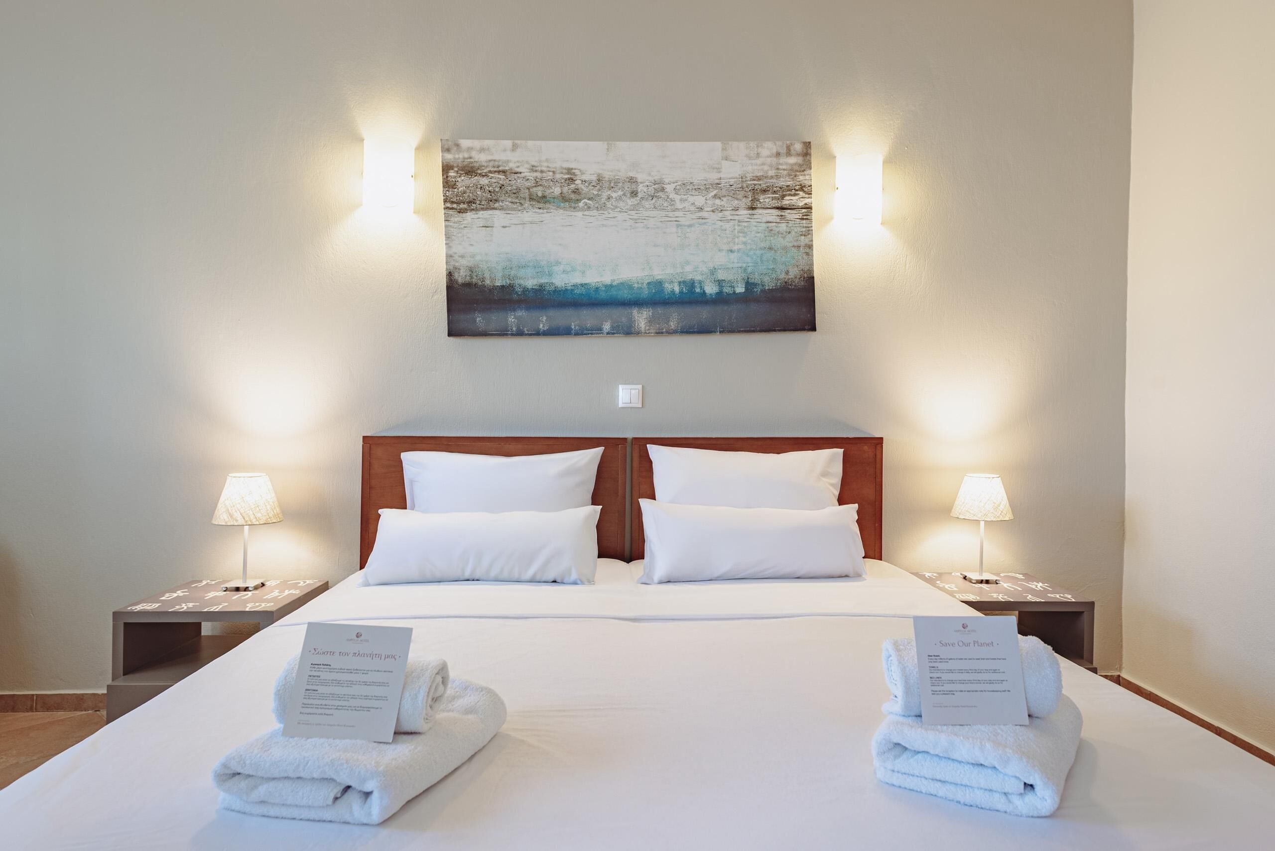 A hotel room with a large bed, two nightstands, a wall-mounted painting, and two lamps.