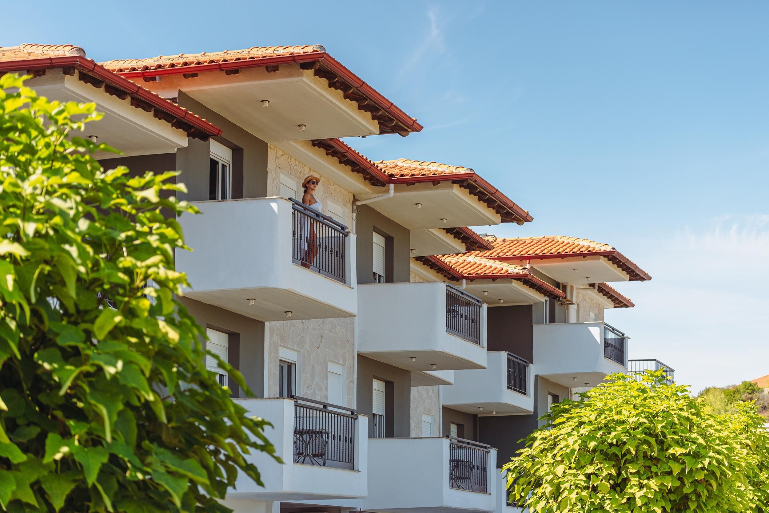 Un edificio residencial de varios pisos con balcones, paredes blancas y techos de tejas rojas.
