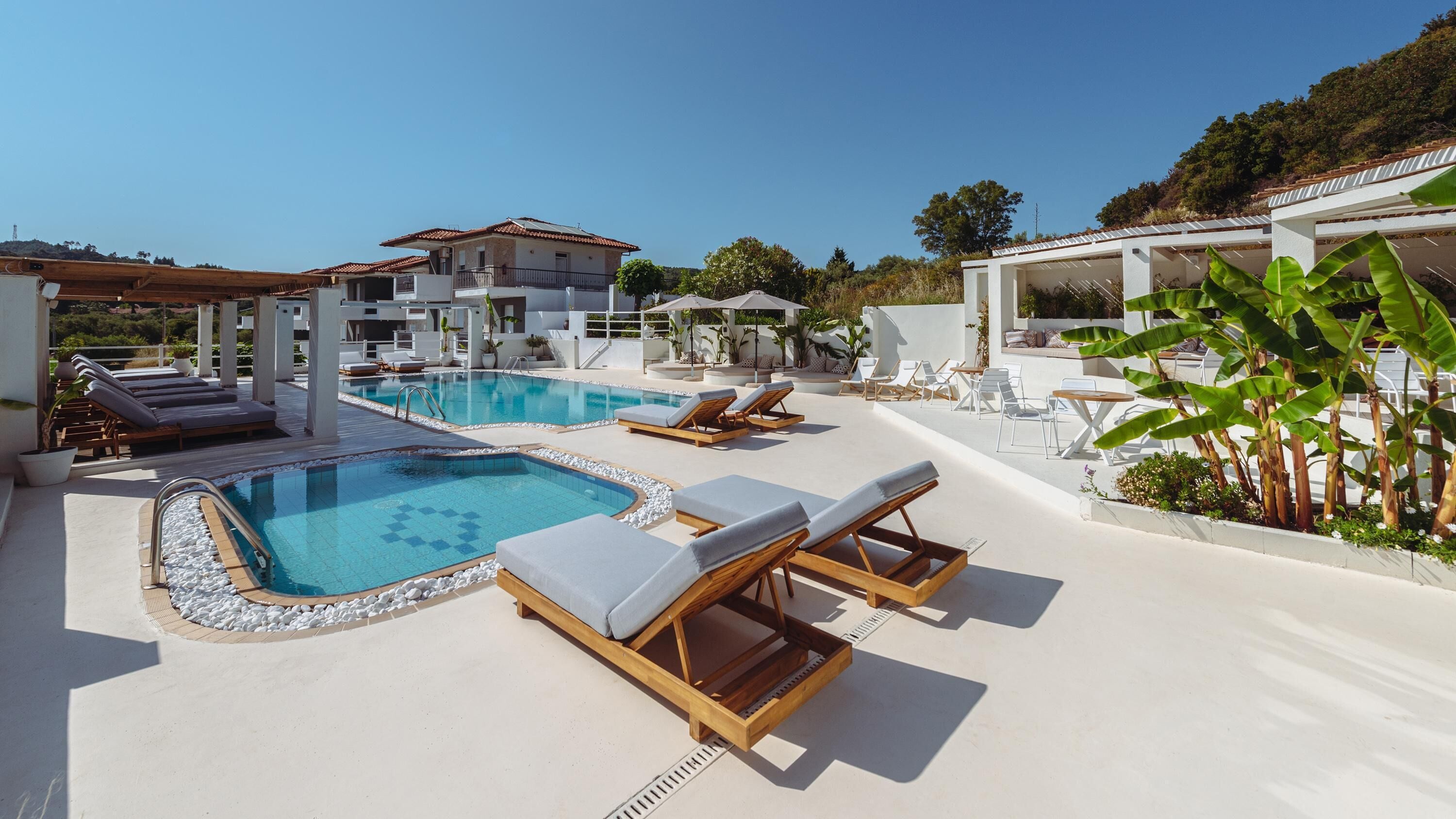 A pool area with lounge chairs, a hot tub, and a view of a hillside.