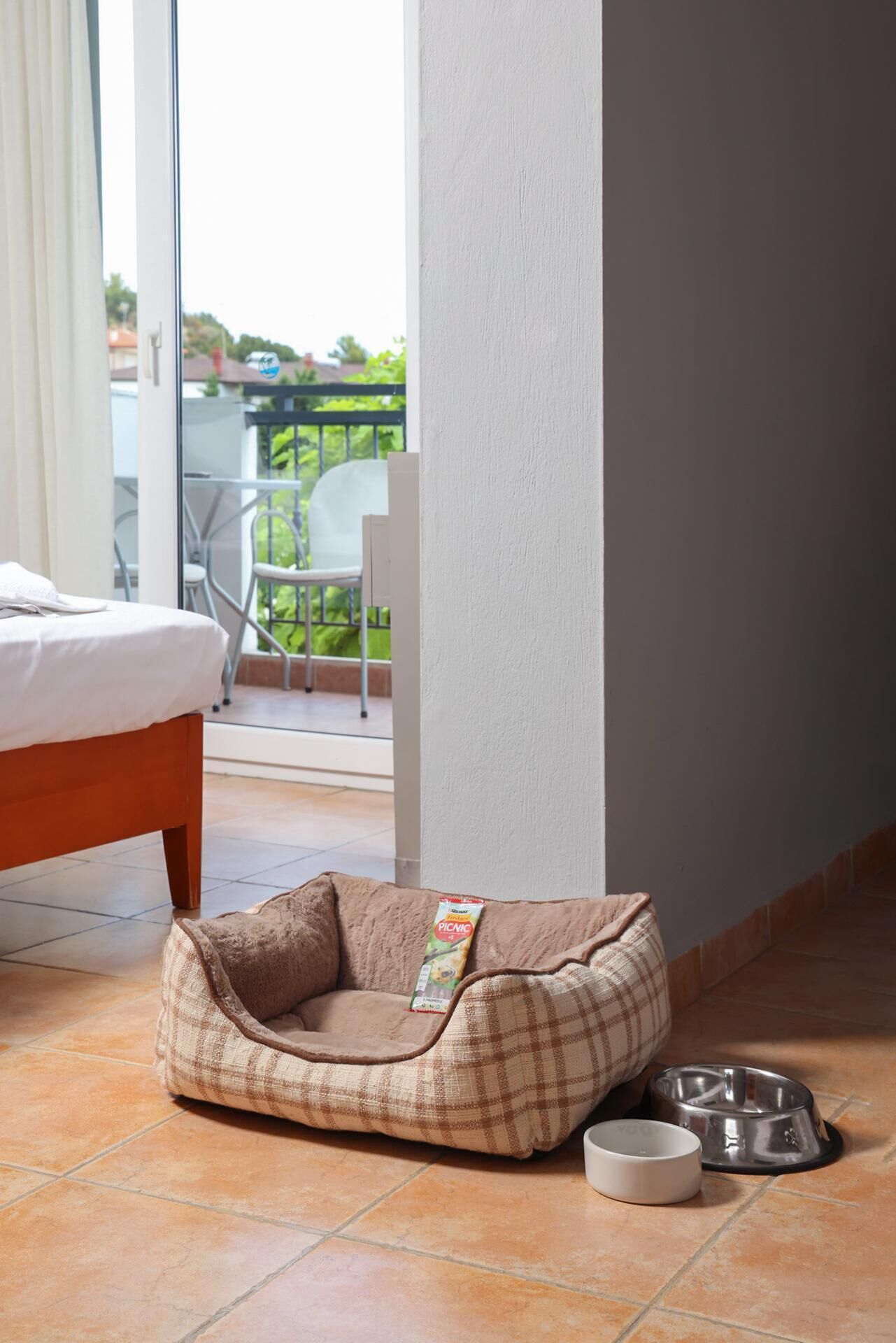 Una cama para mascotas con estampado escocés y un cuenco de metal sobre un suelo de baldosas.