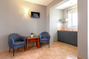 Relax in this cozy space with a flat-screen TV, comfortable armchairs, and a kitchenette with dark grey cabinets.
