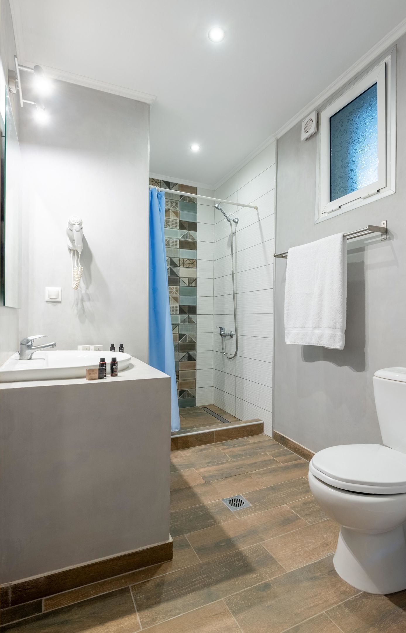 A modern bathroom with a bathtub, shower, toilet, and a window.