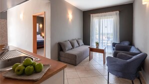 A modern living room with a sofa, a coffee table, and a dining area with a sink and apples on the counter.