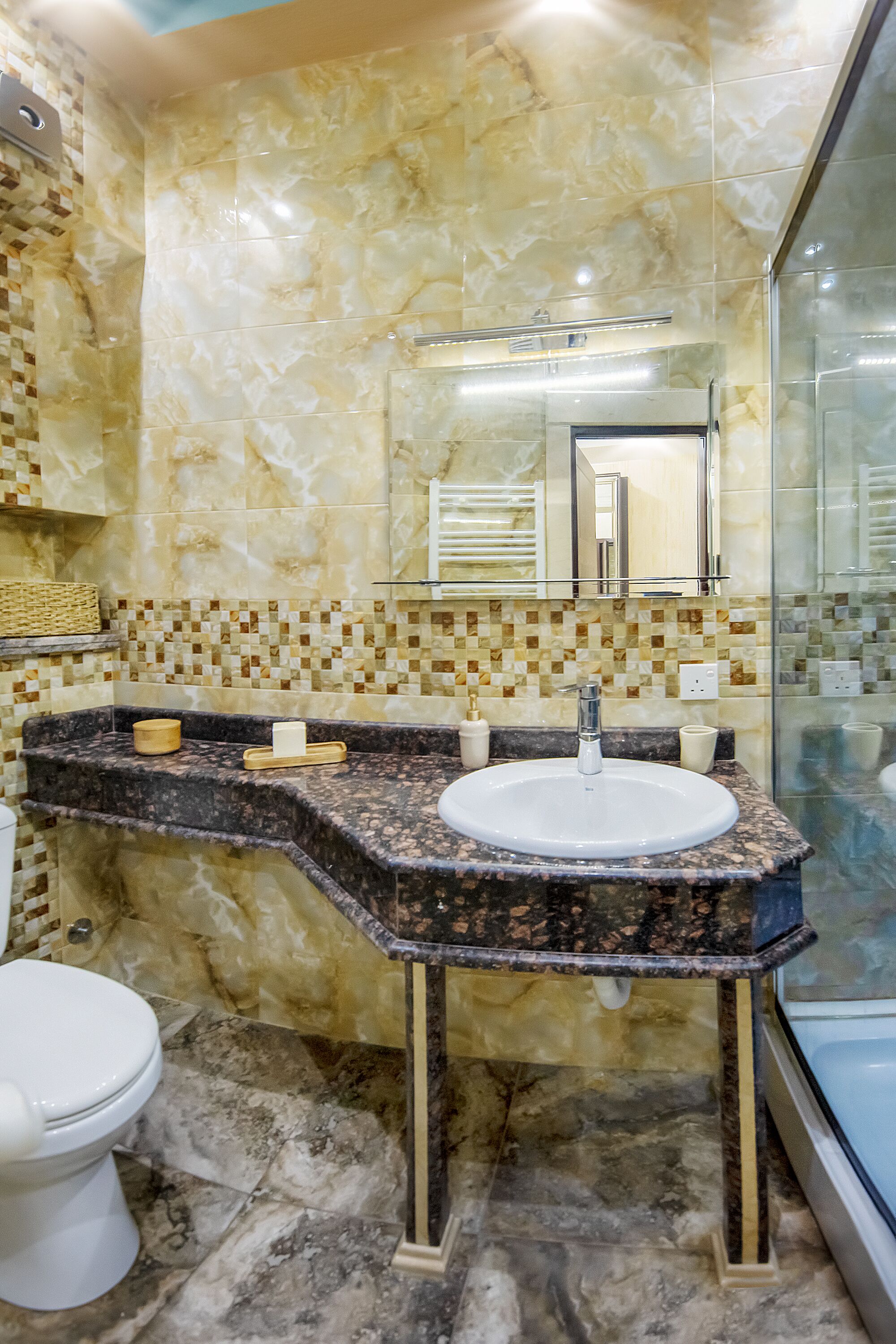 Une salle de bain avec un lavabo en marbre, une douche en verre et un mur recouvert de carreaux.