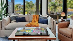 Ein modernes Wohnzimmer mit einer Couch, einem Couchtisch und Blick auf Palmen und Gebäude.