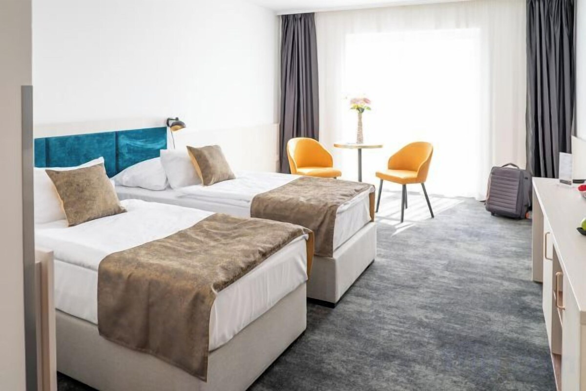 Habitación de hotel con dos camas, un escritorio, una silla y una mesita con un florero.