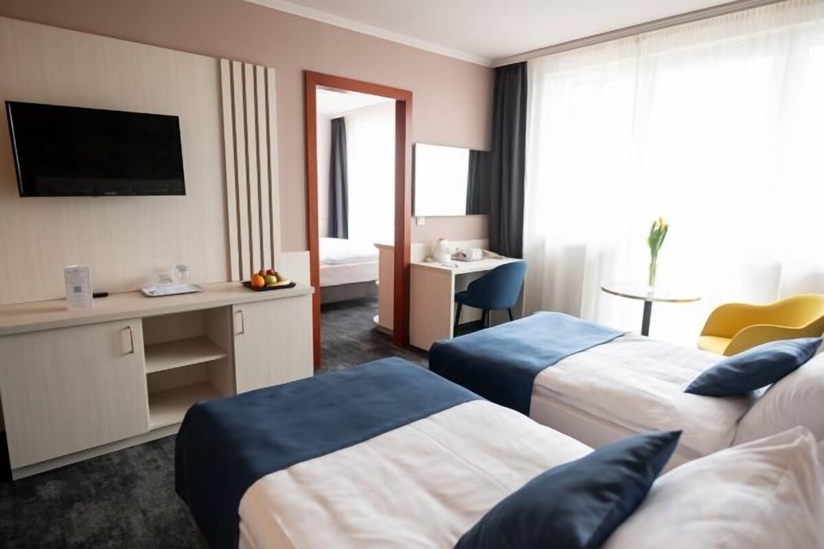 Habitación de hotel con dos camas, un escritorio, un televisor y una pequeña mesa con una planta.