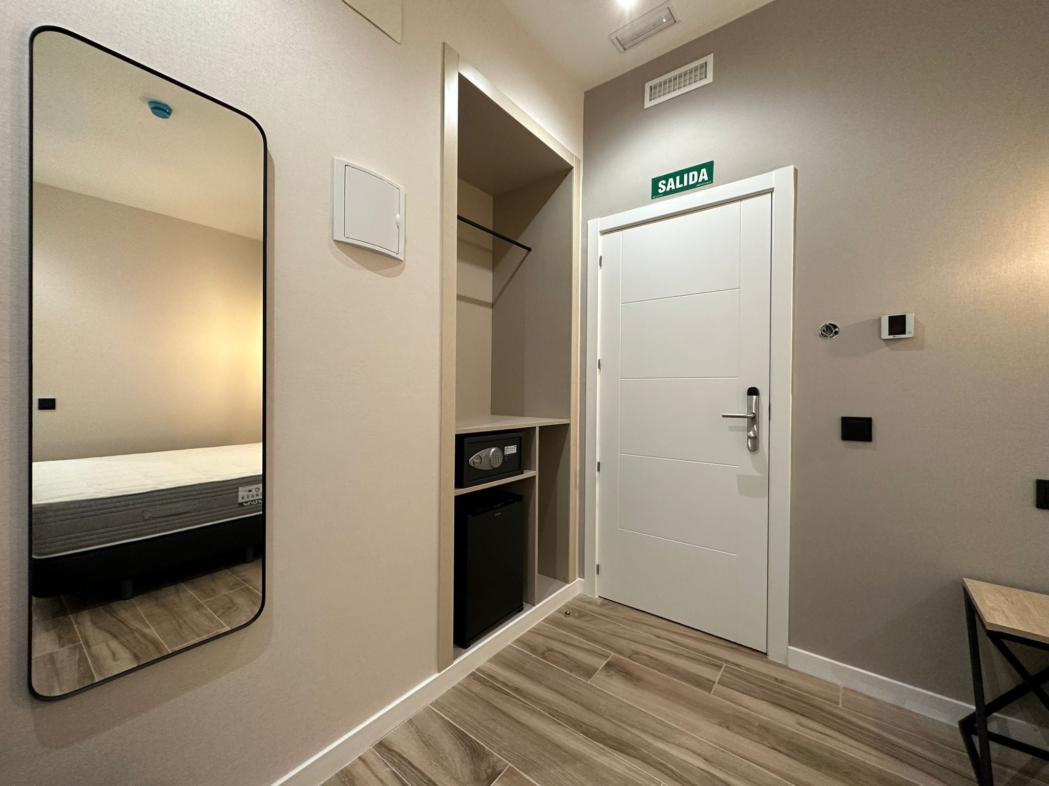 A hotel room with a large mirror, a bed, a wardrobe, a door labeled 'SALIDA', and a small table.