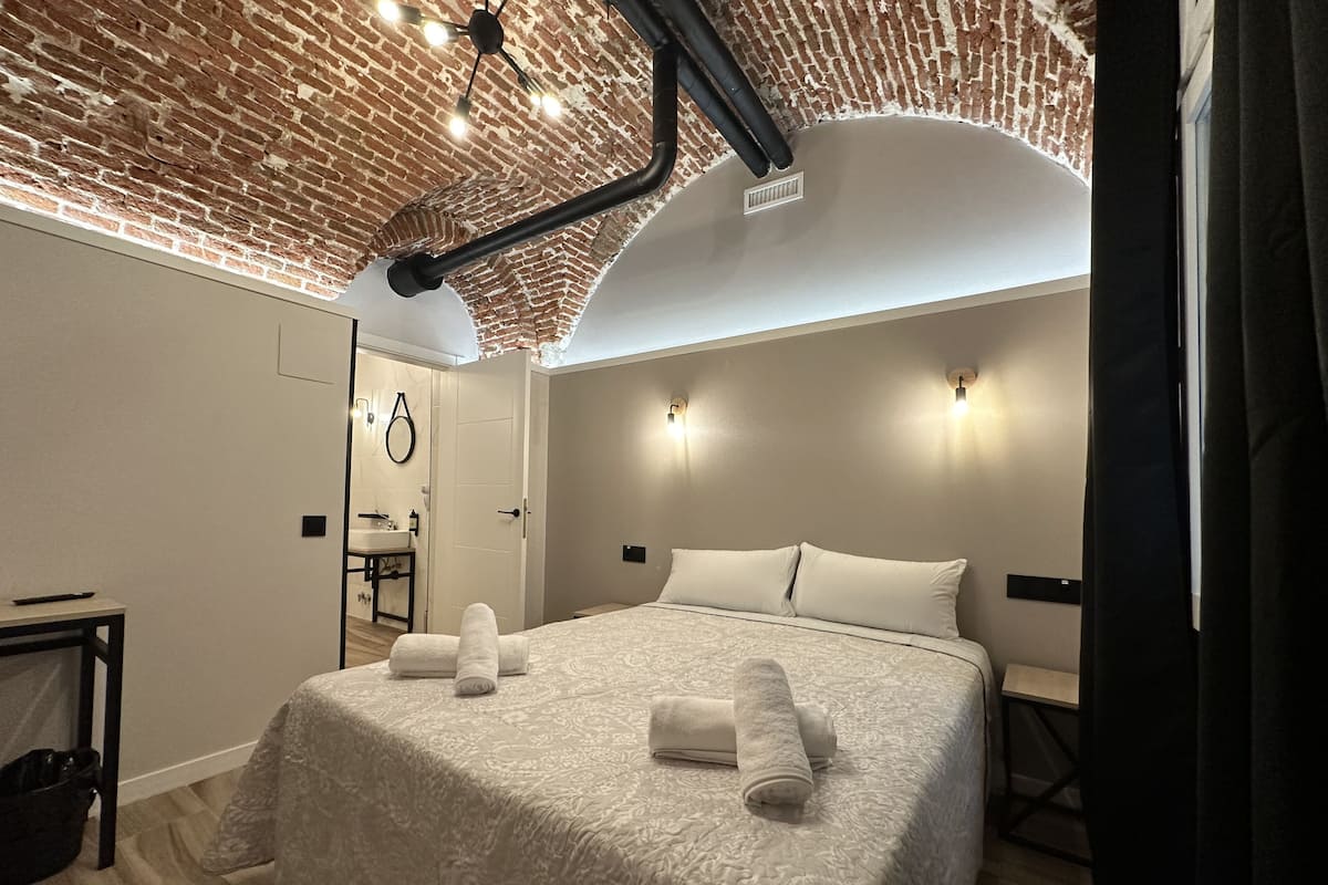 A modern bedroom with a brick ceiling, a large bed with white linens, and two wall-mounted lights.