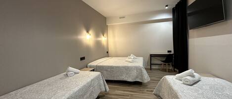 A hotel room with two single beds, a desk, a chair, and a TV mounted on the wall.