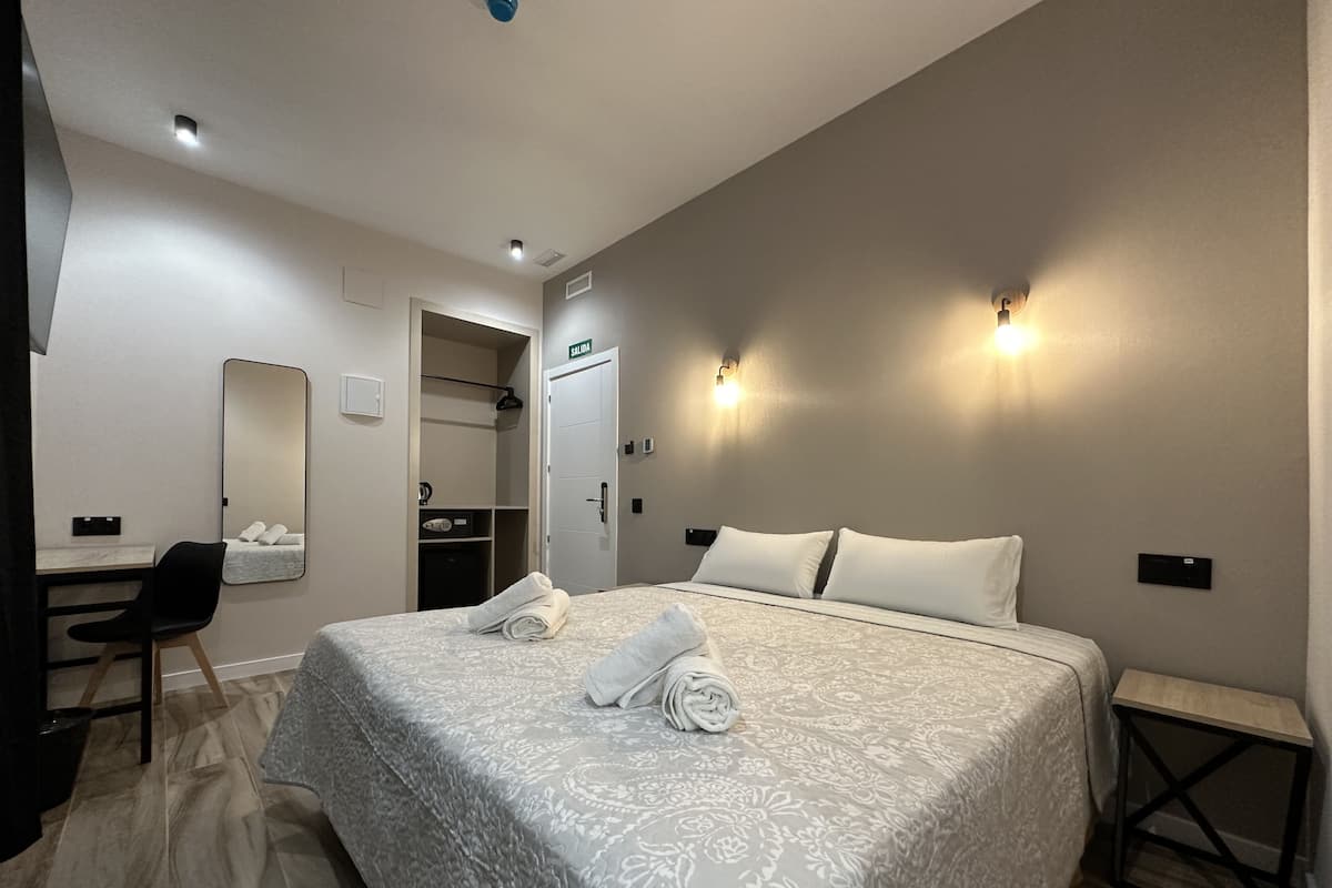 A hotel room with a bed, a desk, a chair, a mirror, and a closet.