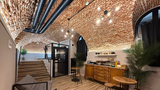 A modern interior with exposed brick walls, a wooden staircase, a kitchen area with bar stools, and a seating area with a coffee table. - CC Opera Suites (Madrid)