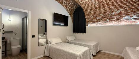 Ein Zimmer mit zwei Betten, einem Fernseher, einer Ziegelwand und Holzboden.