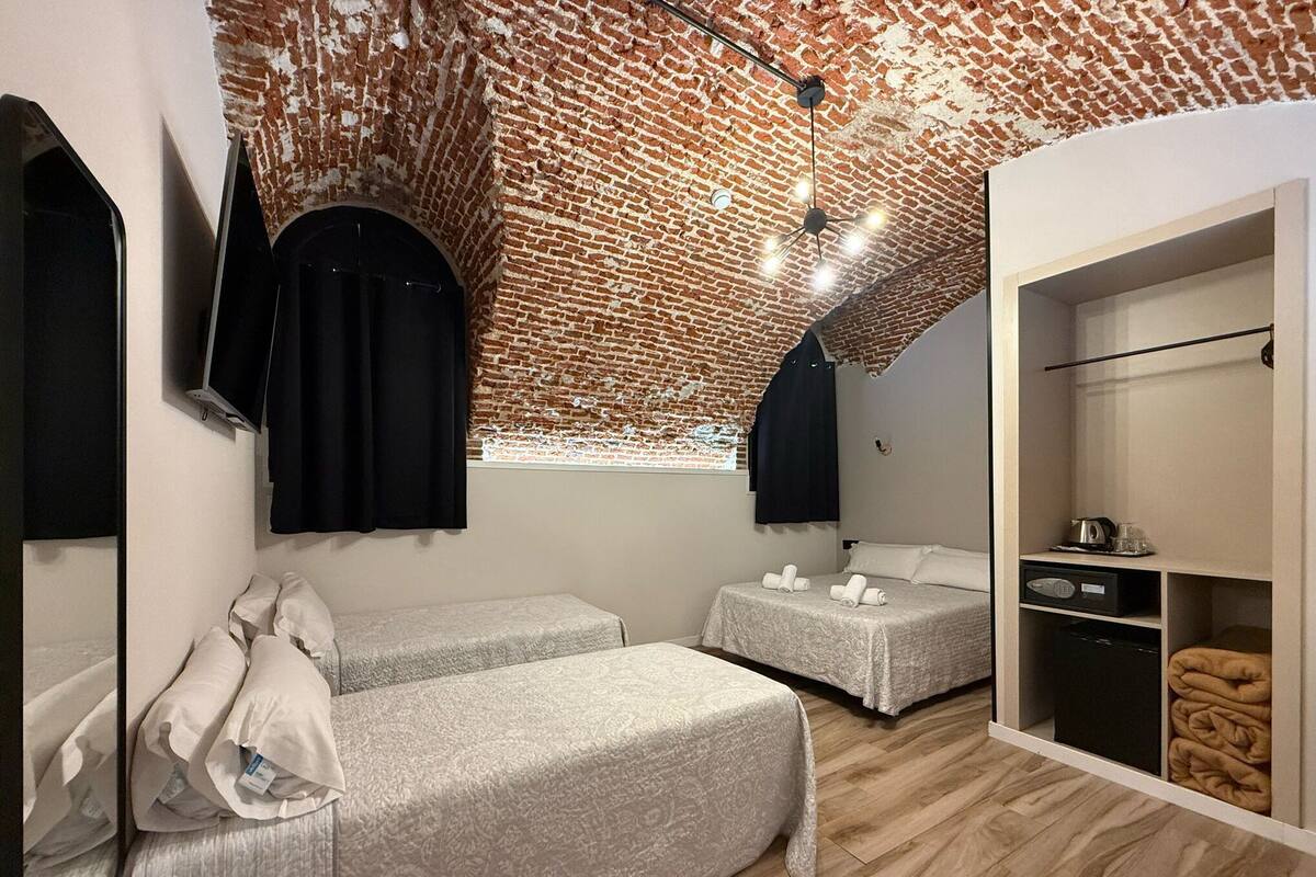 A room with a brick ceiling, two beds, a wardrobe, and a mirror.