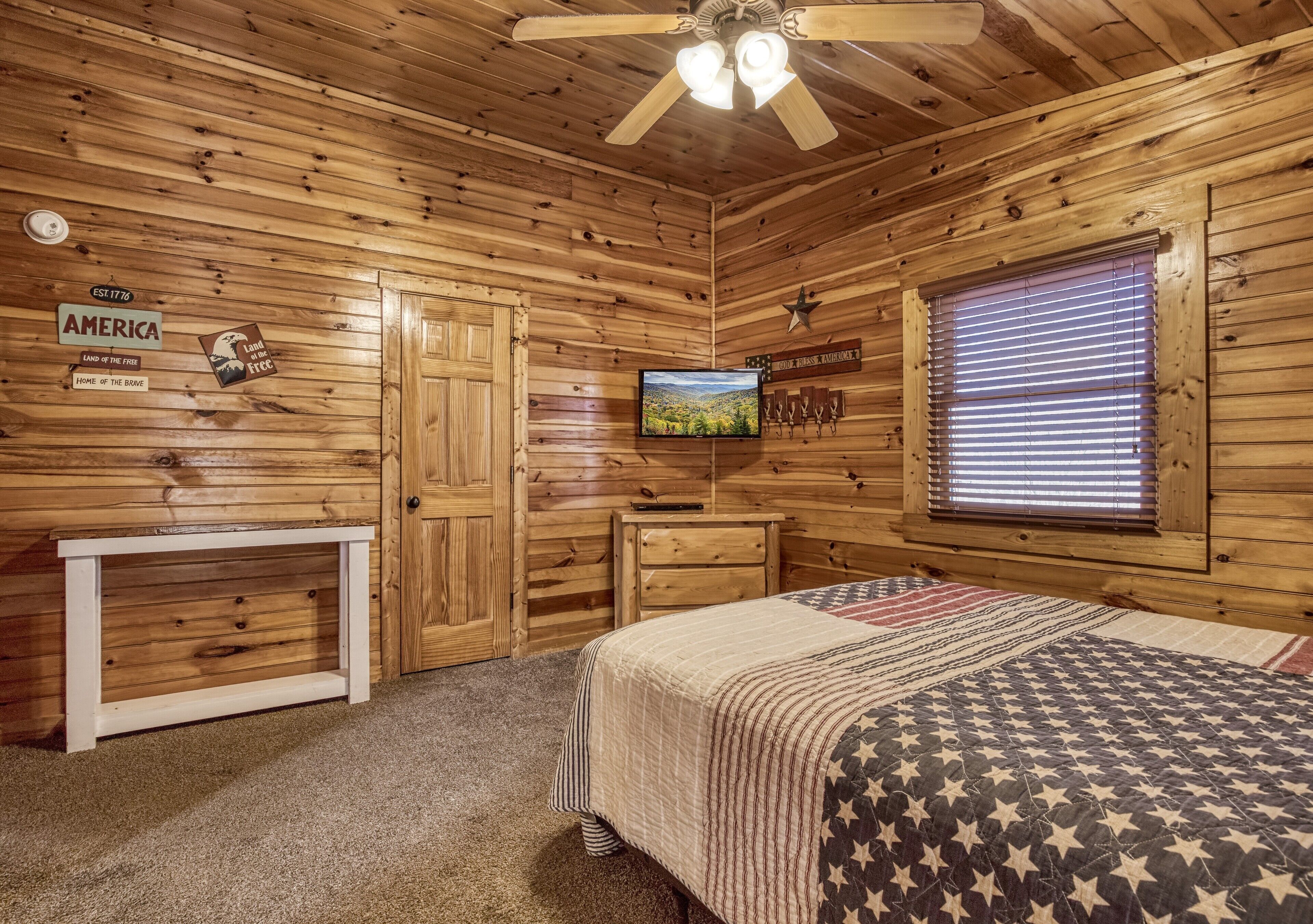 Une chambre de style cabane en bois, équipée d’un lit, d’une télévision, d’un bureau et d’une fenêtre avec des stores.