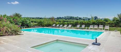 A rectangular swimming pool with a small hot tub, surrounded by lounge chairs and greenery.