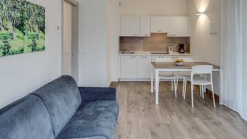 A modern kitchen with white cabinets, a dining table with chairs, and a gray sofa in a living area.