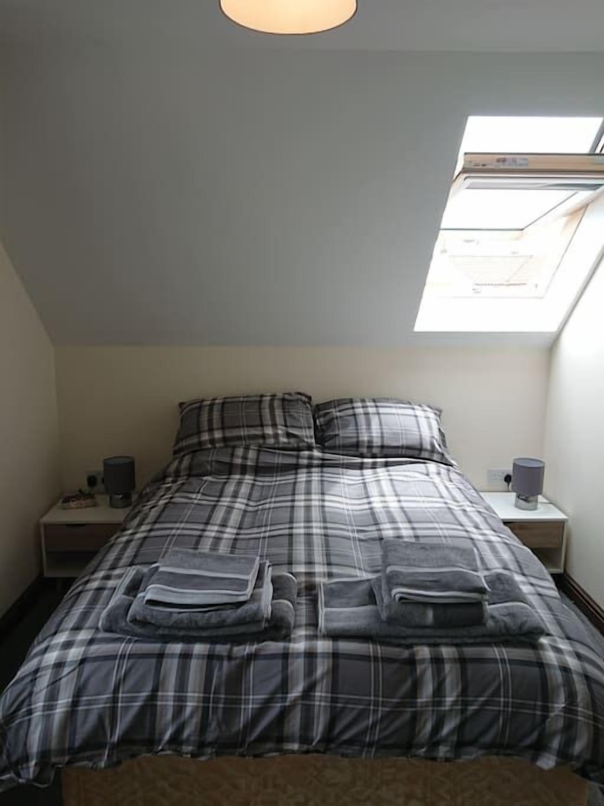 A bedroom with a bed, a nightstand, a lamp, and a skylight.