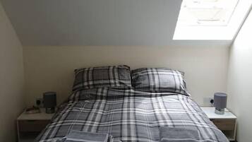 A bedroom with a bed, a nightstand, a lamp, and a skylight.