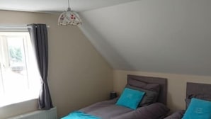 A bedroom with two beds, a window with curtains, a radiator, and a ceiling light fixture. - 1 Wood Yard Cottages. 2 Bedroom, Large lounge (Long Sutton)