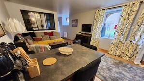 Una sala moderna con comedor, un conjunto de sofás, un televisor de pantalla plana y un amplio ventanal con cortinas.