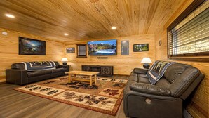 Un accogliente soggiorno con pareti e soffitto in legno, due divani in pelle, un tavolino in legno e un'ampia televisione a schermo piatto.