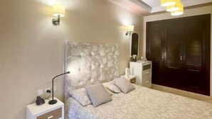 Quarto com colcha estampada, luminárias de cabeceira, mesa de cabeceira, cômoda e guarda-roupa.