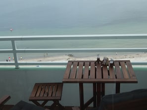 Une table et un banc en bois sur un balcon donnant sur une plage où se trouvent des gens et un poste de surveillance des sauveteurs.