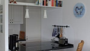 Una cocina compacta con armarios blancos, encimera negra y un pequeño comedor con una silla de mimbre.