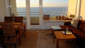 Un salón acogedor con una mesa de madera, un sofá y vista al mar a través de un ventanal.