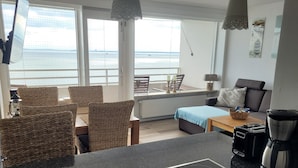Una cocina moderna con estufa integrada, comedor con sillas de mimbre y vista al mar a través de amplias ventanas.