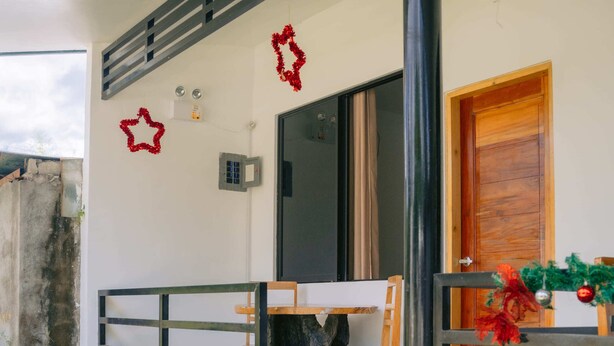 A modern house with a wooden door, a small porch with a table and chairs, and a potted plant. - L'Puerta Travel Inn (Hinoba-an)