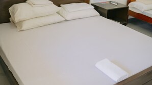 A neatly made bed with white linens and pillows, a wooden headboard, and a bedside table with a remote control. - L'Puerta Travel Inn (Hinoba-an)