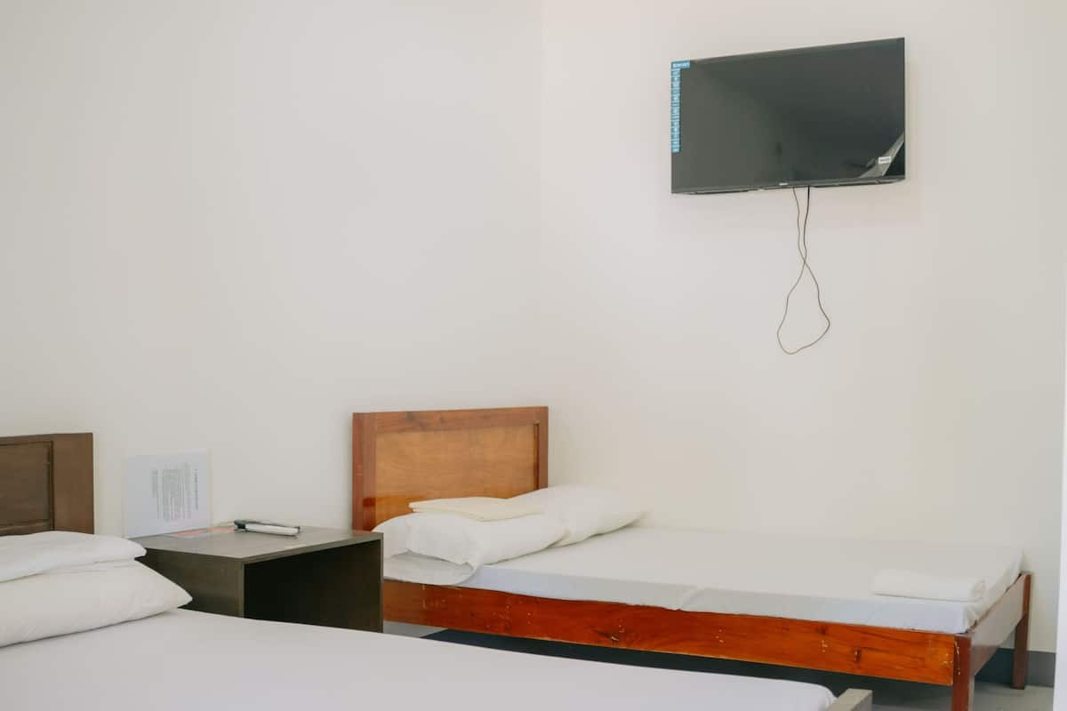 A hotel room with two beds, a flat-screen TV mounted on the wall, a nightstand, and a wooden headboard.