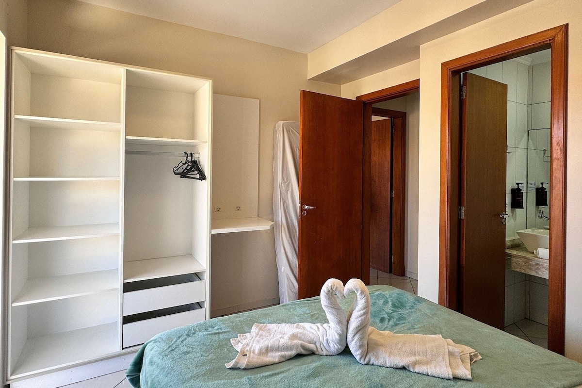 Habitación de hotel con cama, armario y baño visible a través de una puerta abierta.
