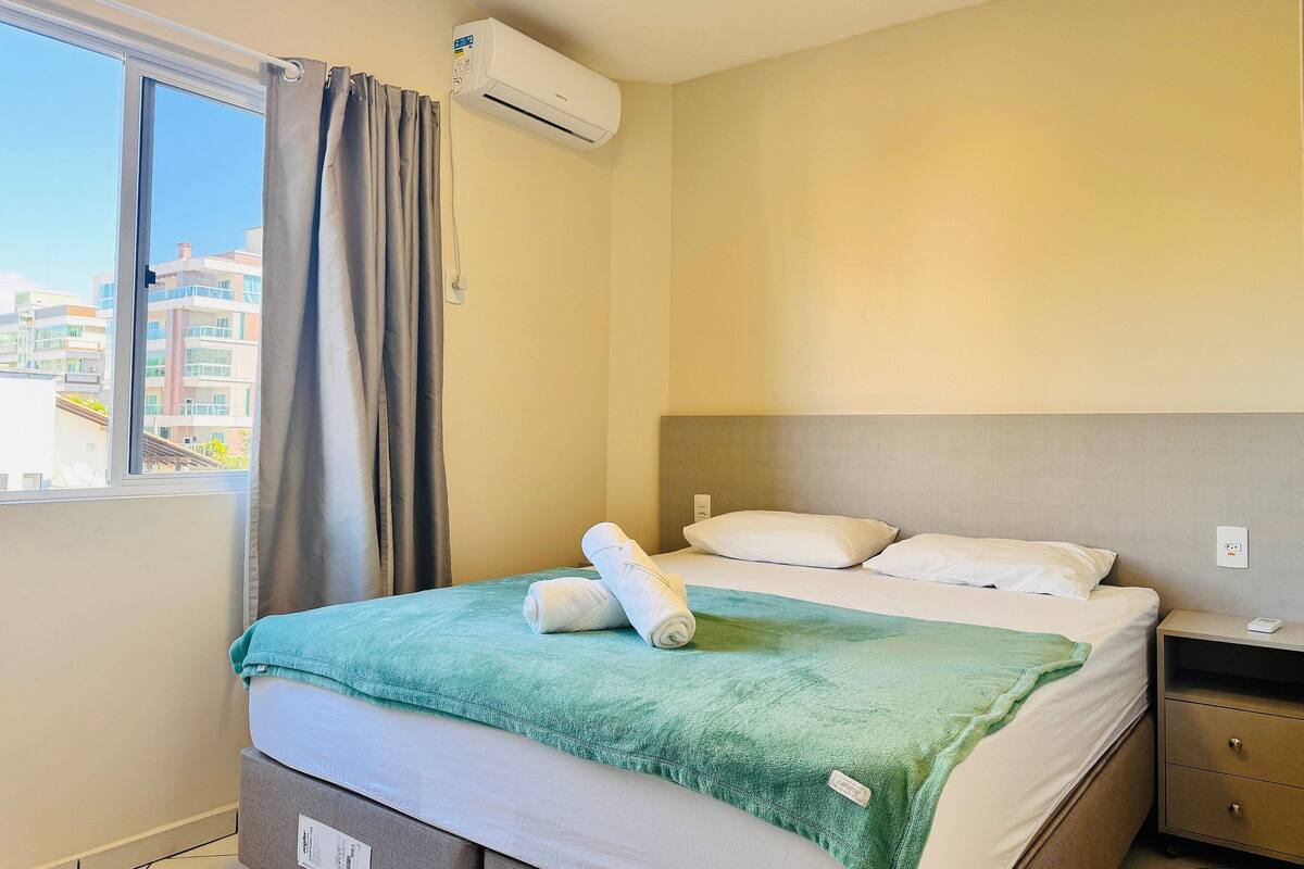 Una habitación de hotel con una cama, una mesita de noche, una ventana con cortinas y un equipo de aire acondicionado.