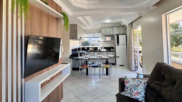 A modern kitchen with a dining area, a TV mounted on the wall, and a ceiling fan. - Canto do Corrupião (Bombinhas)
