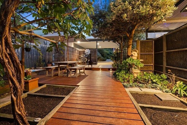 Stroll through the serene garden, surrounded by lush greenery and a tranquil seating area with a bench and dining table.