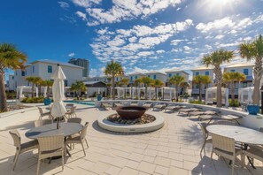 A poolside area with lounge chairs, a fire pit, and palm trees.