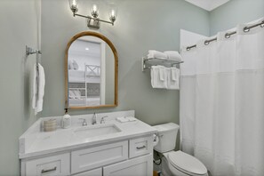 A bathroom with a white vanity, a toilet, a shower curtain, and a mirror with a wooden frame.