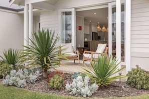 Een modern huis met een patio, compleet met een eettafel en stoelen, omgeven door diverse planten en een verzorgde tuin.