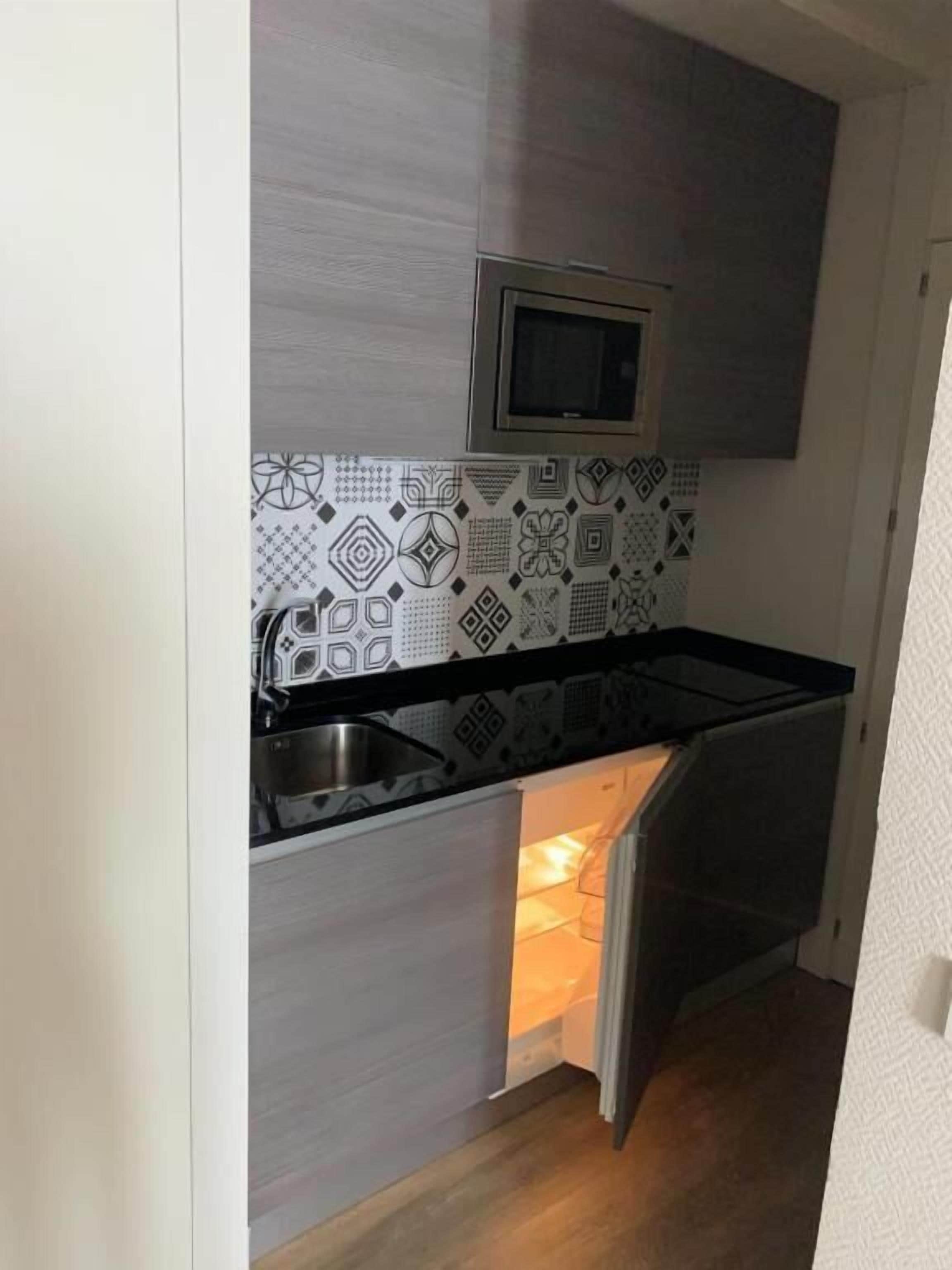 A compact kitchen with a built-in microwave, a stainless steel sink, and patterned backsplash tiles.