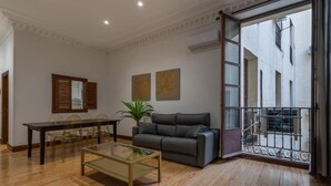 Un salón amplio con suelo de madera, una mesa de centro de cristal, un sofá gris y un comedor con mesa y sillas de madera.