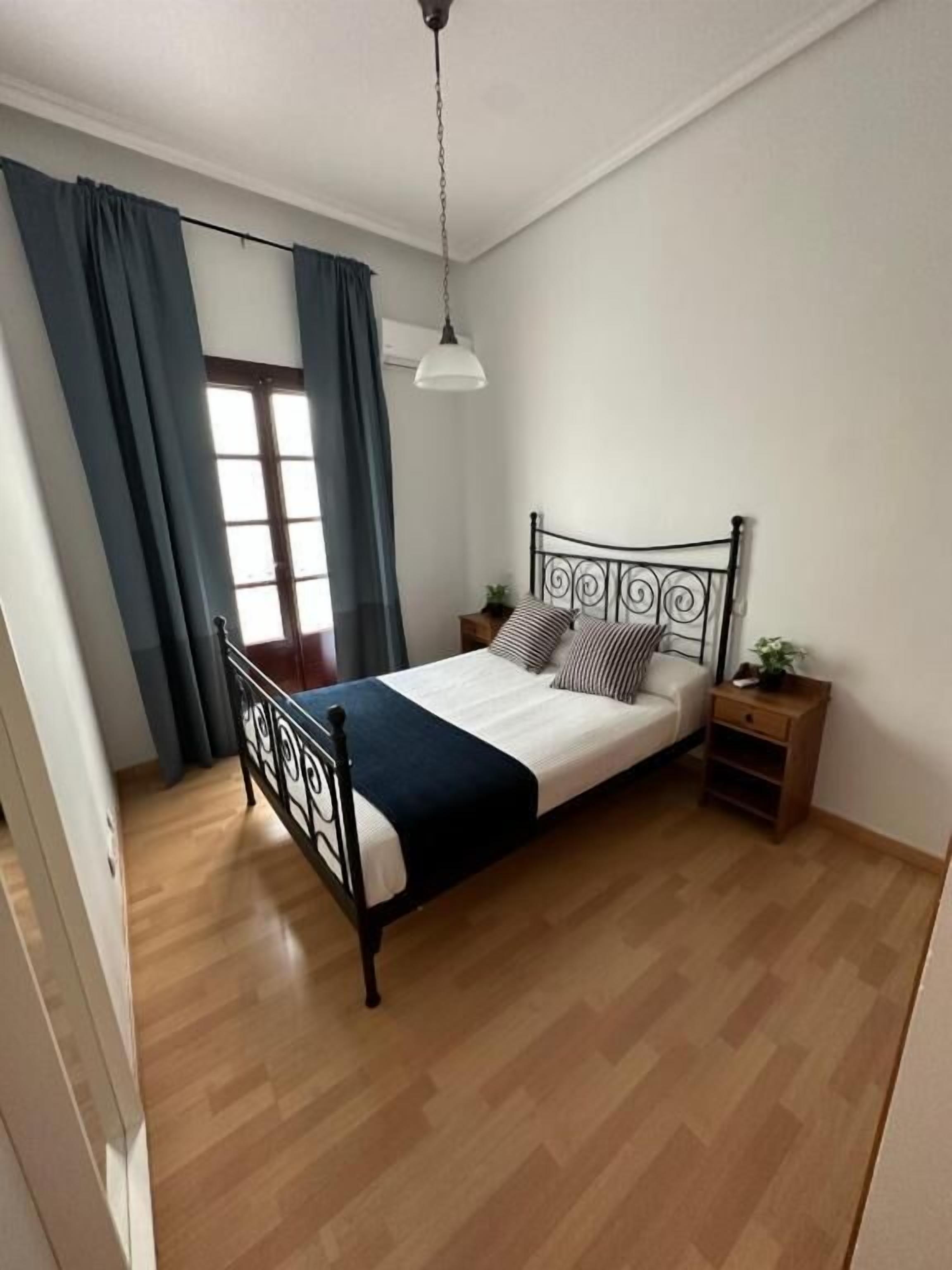 A bedroom with a bed, a nightstand, a hanging light, and a window with curtains.